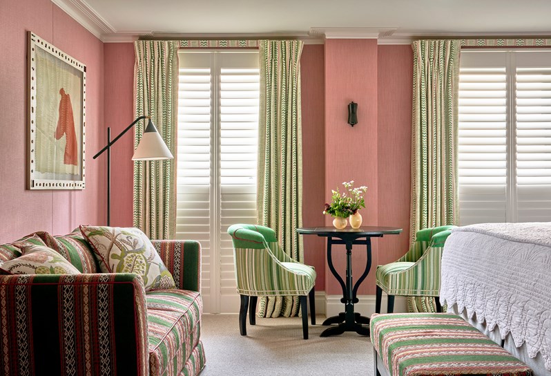 Side bedroom shot a deluxe room, 005, at Knightsbridge Hotel with plain light pink walls and two green chairs and a black desk as well as a sofa and a long chair with green and pink stripes.