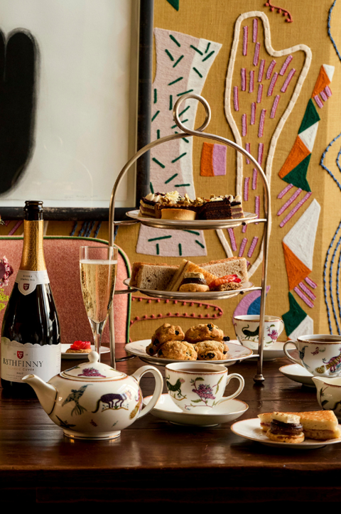 A portrait shot of the Afternoon Tea in the Dora Carrington Room at Charlotte Street Hotel: There are two afternoon tea stands on the table being served with a bottle of sparkling wine