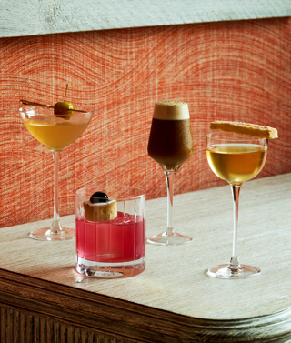 An image of 4 cocktails against a red fabric wall. 3 martini shaped glasses and one short whisky glass. 