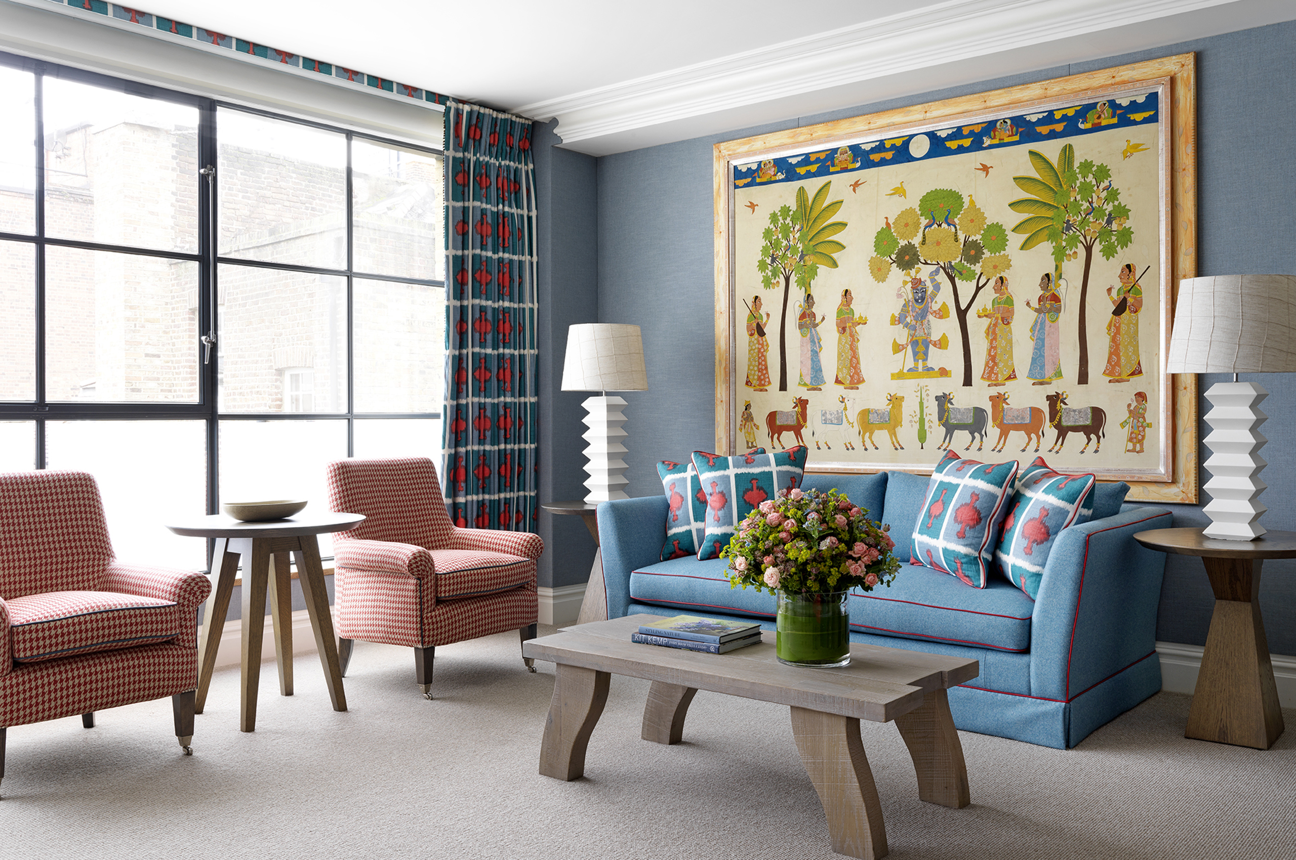 Elegant hotel suite with blue sofa, red chairs, and framed artwork