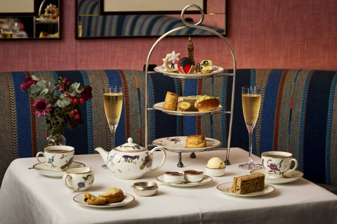 This is an image of the Christmas London Calling festive afternoon tea offering at Brumus at Haymarket Hotel. This image shows a table in Brumus set with Mythical creatures crockery and the full afternoon seat set up including pots of tea, tea cups, champagne and a stand with sandwiches, scones with preserves and cakes all in a festive and classically British theme. 
