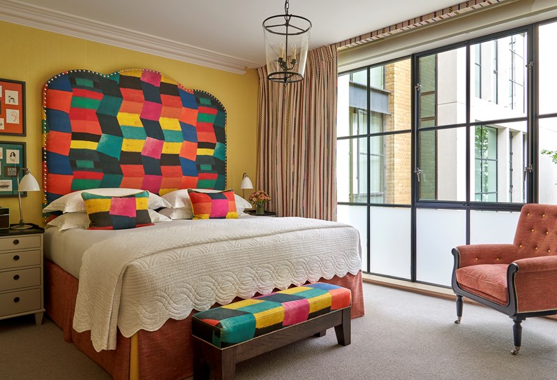 A bedroom at Ham Yard Hotel with a multicoloured statement headboard and floor-to-ceiling crittal-style windows