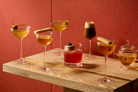 An image of five cocktails. 4 tall martini shaped glasses and one short whisky glass. And a glass pot of rose tea cordial. In front of a red fabric wall. 