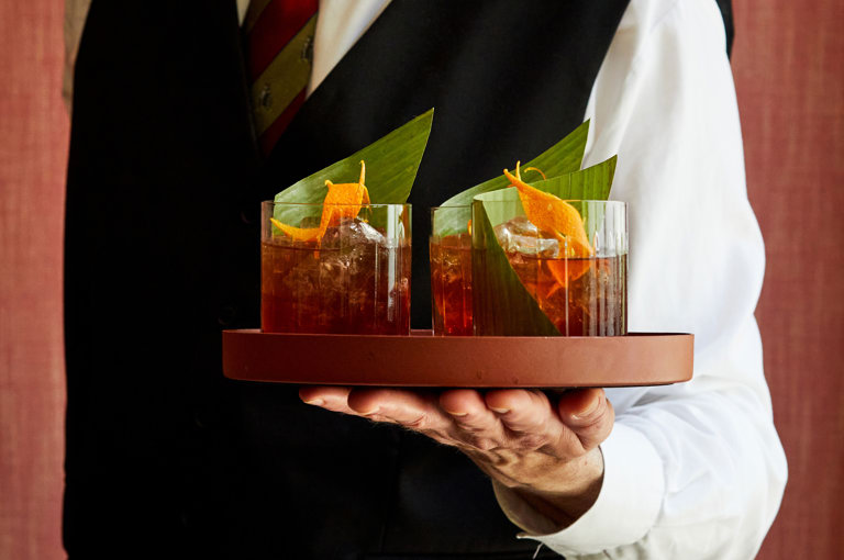 A male member of staff holding a tray of three You take the high road…cocktails at Refuel, The Soho Hotel. 