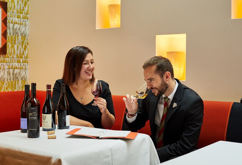 Head of F&B, Sarah Williams and Wine Supervisor, Lawrence Rugeroni tasting wines sat on banquette seating behind a table with four bottles of wine in front of them