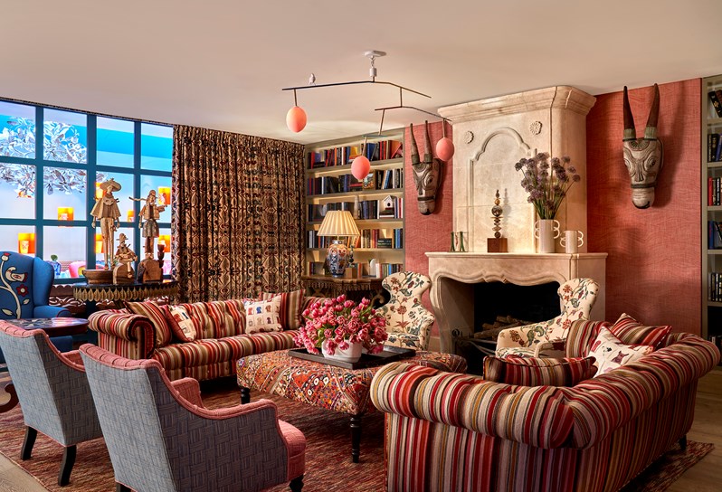 The Drawing Room at Warren Street Hotel with two sofas upholstered in a dark red striped fabric, a large rectangular footstool in a red embroidered fabric and two curvaceous statement armchairs in a cream, red and blue floral fabric