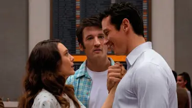 A still from Eternity. A woman looks up at a man opposite her, who is smiling and holding her hand. Behind them, another man stands looking concerned