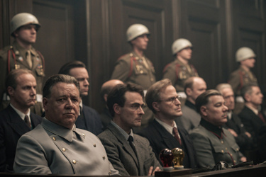 A still from Nuremberg. Rows of Nazi men are seated looking solemn 