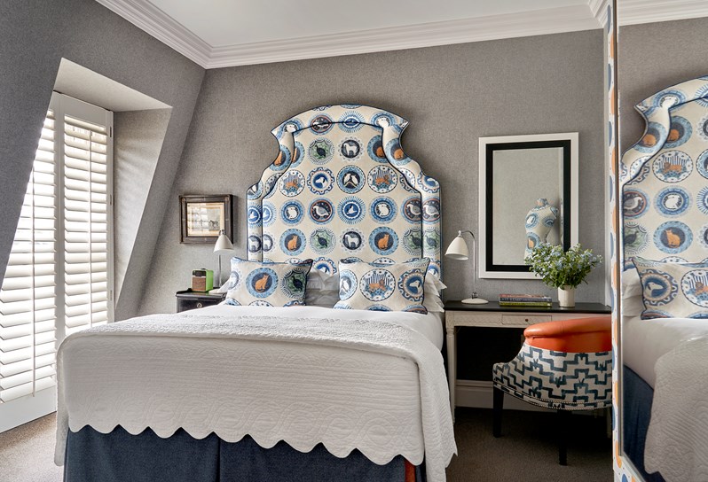 Front bedroom shot a deluxe room with plain light grey walls, colourful animal drawings on the headboard and the pillows with blue tones and a chair and desk next to the bed.