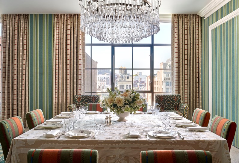 A dining table set up for 8 people, shot looking down the table onto views of New York from floor to ceiling windows.