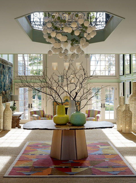 A double height hallway with a organic wood table and statement light fitting hung above