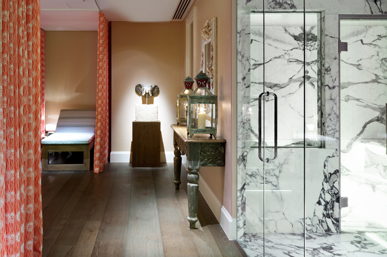 An image of the Soholistic Spa interior, on the left a relaxation lounger, an elephant sculpture on a pedestal, on the right a glass door leads into a white marble steam room.