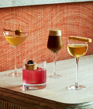 An image of four cocktails , three tall martini shaped glasses and one short whisky glass, against a fabric orange backdrop.