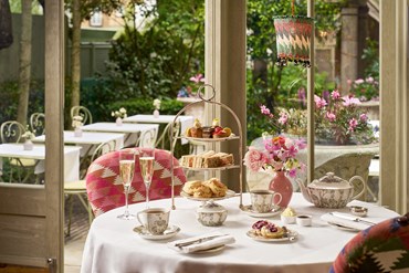 Champagne afternoon tea displayed on a table in the Orangery looking on to the garden at Number Sixteen hotel. The fine bone china is Mythical Creatures by Kit Kemp for Wedgwood along side a 3 tier cake stand, sandwiches and scones.