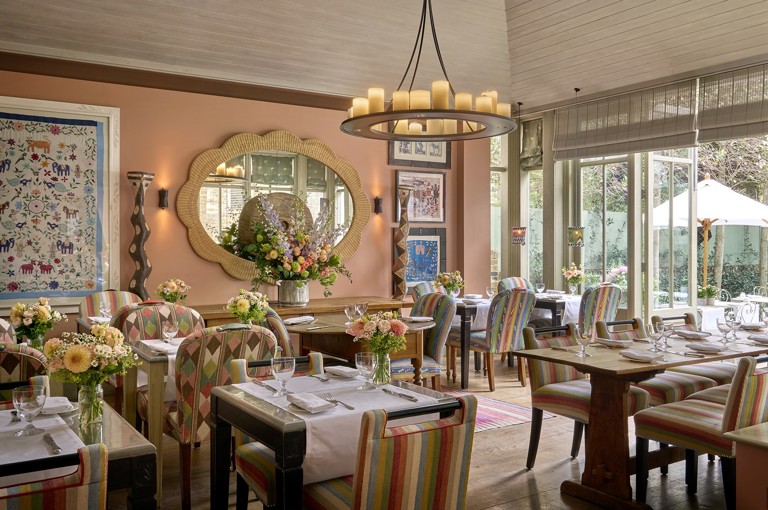A wide view across The Orangery restaurant at Number Sixteen hotel, looking through to the garden beyond. The restaurant tables are laid with crockery, cutlery and glassware.