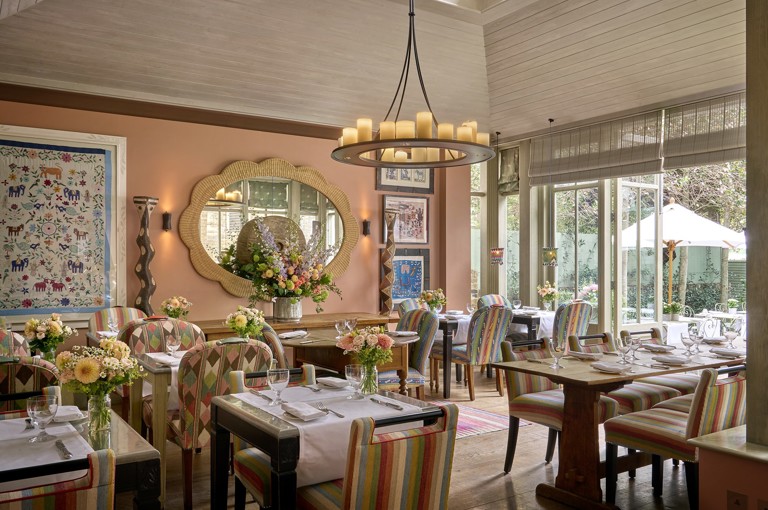 A wide view across The Orangery restaurant at Number Sixteen hotel, looking through to the garden beyond. The restaurant tables are laid with crockery, cutlery and glassware.