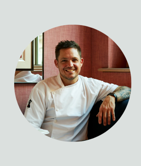 A circle crop of a headshot of Head Chef Richard Wilkins sat in his chef whites
