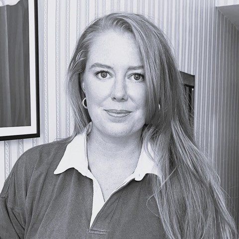 A portrait black and white headshot of costume designer Grace Snell. She has her hair down and is wearing a collared sweatshirt