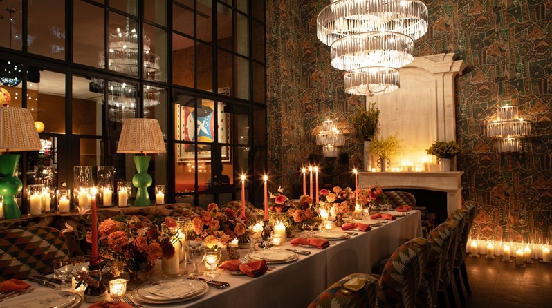 Image of a long table set up for dinner with dim candle lighting in The Orangery at Crosby Street Hotel.