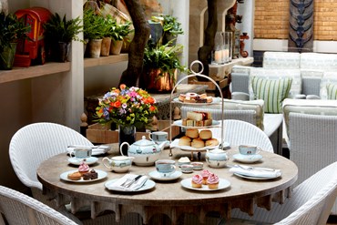 Afternoon tea displayed on a table in Ham Yard restaurant. The fine bone china is Mythical Creatures by Kit Kemp for Wedgwood along side a 3 tier cake stand, sandwiches and scones.