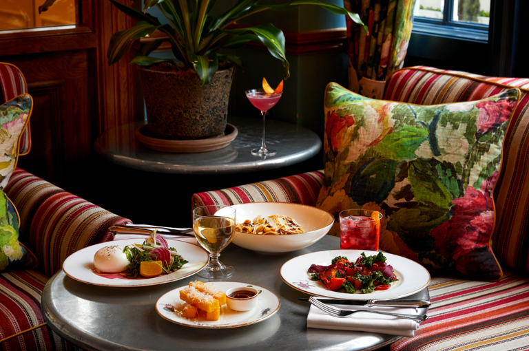 An image of the table in the Oscar Bar at Charlotte Street Hotel. Featuring, multiple plates from the bar food menu.  Including - Roasted vegetables, Burrata Salad and Pasta dish. 