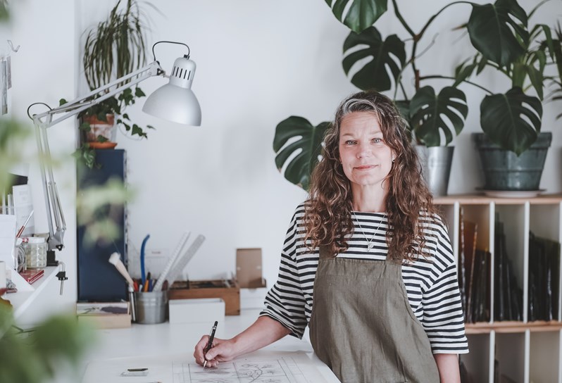An image of Flora Jamieson in her studio designing her stained glass artwork, this image is used to promote her stained glass workshop at Haymarket Hotel.
