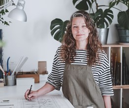 An image of Flora Jamieson in her studio designing her stained glass artwork, this image is used to promote her stained glass workshop at Haymarket Hotel.