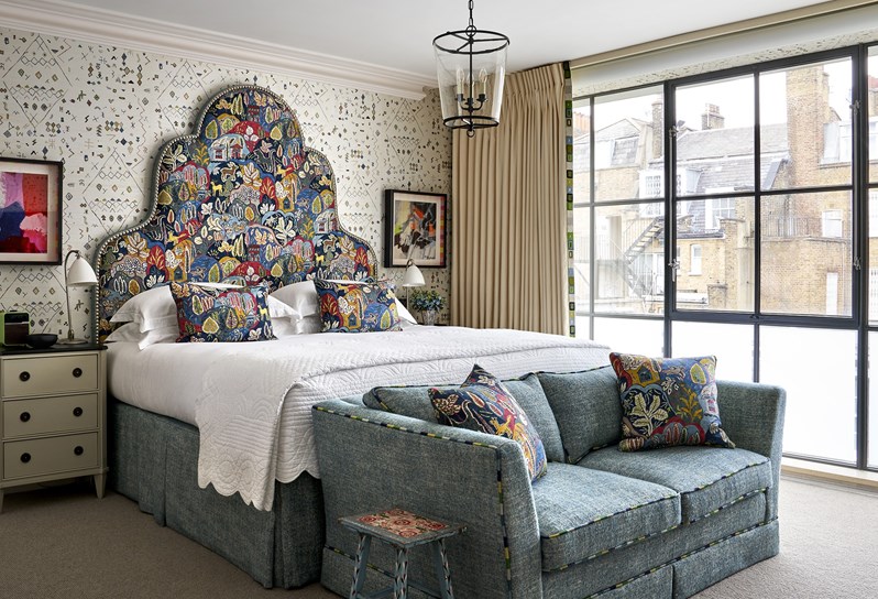 A room at Ham Yard Hotel with a large statement headboard and a sofa at the end of the bed
