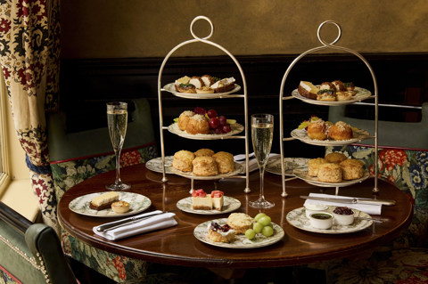 A wide shot of the items in Afternoon Cheese at Brasserie Max at Covent Garden Hotel. At the table, there are two stands holding plates of scones and cheese-inspired pastries, served alongside two glasses of Champagne. 
