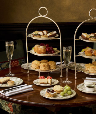 A wide shot of the items in Afternoon Cheese at Brasserie Max at Covent Garden Hotel. At the table, there are two stands holding plates of scones and cheese-inspired pastries, served alongside two glasses of Champagne.