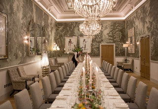 Wide shot of a long dining table dressed with colourful flowers and tall candlesticks in the Shooting Gallery private events room at Haymarket Hotel