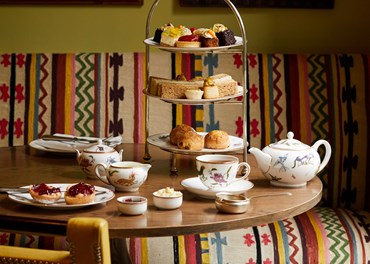 Champagne afternoon tea displayed on a table in The Potting Shed restaurant at the Dorset Square Hotel. The fine bone china is Mythical Creatures by Kit Kemp for Wedgwood along side a 3 tier cake stand, sandwiches and scones.