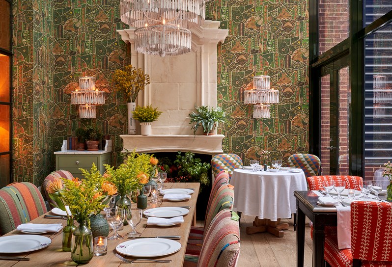 Shot of the Orangery facing the wall with the fire place and chandeliers and the curtain wall on the right. There three tables set up including one large table in the middle of the room and front left of the shot.
