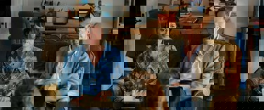 A still from 'The Roses'. A middle-aged couple played by Olivia Coleman and Benedict Cumberbatch, sit on a brown sofa looking at a woman opposite them, who is out of view.