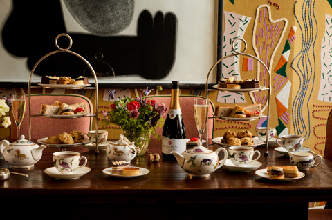 A wide shot of the Afternoon Tea in the Dora Carrington Room at Charlotte Street Hotel: There are two afternoon tea stands on the table being served with a bottle of sparkling wine