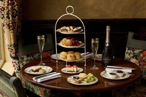 A wide shot of the items in Afternoon Cheese at Brasserie Max at Covent Garden Hotel. At the table, there is a stand holding plates of scones and cheese-inspired pastries, served alongside a bottle of Champagne.