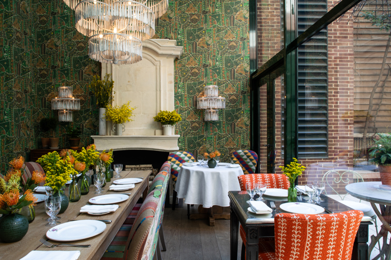 Restaurant set up in the Orangery at Crosby Street Hotel. Shot looking down a long table with two smaller tables to the right