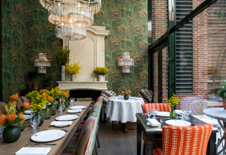 Restaurant set up in the Orangery at Crosby Street Hotel. Shot looking down a long table with two smaller tables to the right