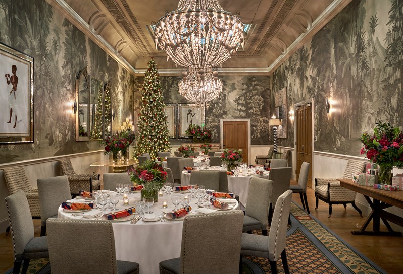 A Christmas dining setup in round tables for eight people with crackers on each plate. The Shooting Gallery has a chandelier hanging from the centre with a Christmas tree in the corner.