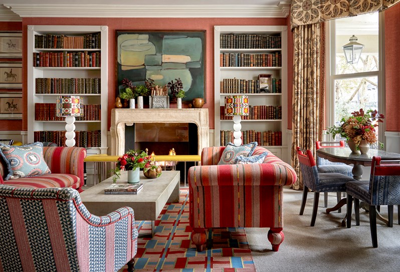 Two sofas placed opposite each other with a low coffee table between, arranged in front of a fireplace which has book cases on both sides. On the right there is also a dining table and chairs in front of large windows.