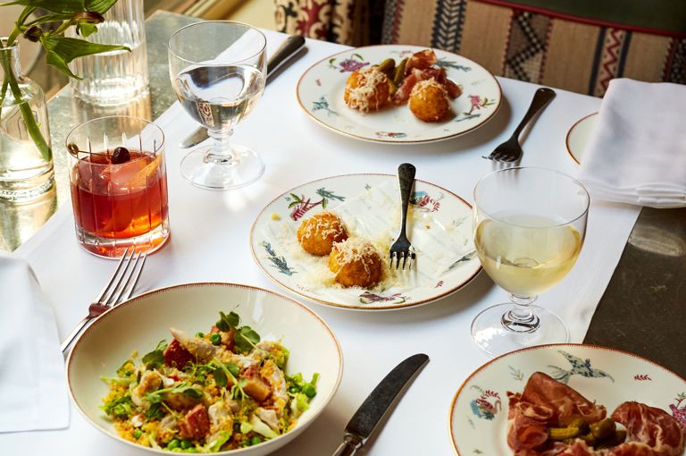 Wide shot of bar food on a table at Brasserie Max. Plates of ham, arancini and salad