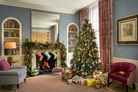 The drawing room of the Townhouse at Haymarket Hotel decorated for Christmas. There is a garland and stocking hanging over the fireplace and a decorated Christmas tree with presents underneath by the window