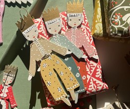 Two portrait images stitched together. On the left, a painted soldier decoration laid on a table surrounded by candlesticks and ribbon. On the right, two small decorations depicting women in coloured outfits and crowns laid on a wrapped box.