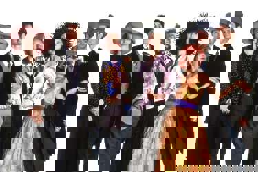 The key characters of Four Weddings and Funeral. Four men stand in coats and tails and three women wear dresses and hats ready for a wedding