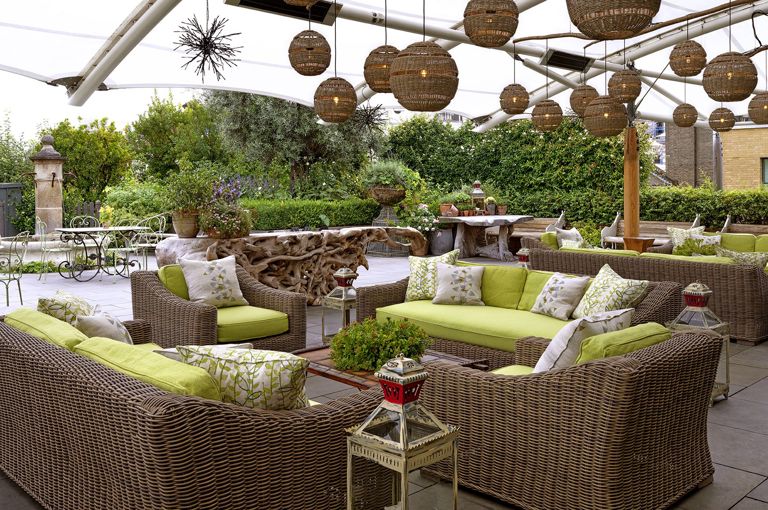 Diagonal shot from the bar of the Roof Terrace at Ham Yard Hotel, it shows the lime green cushioned and wicker sofa seating area with a coffee table in the centre.