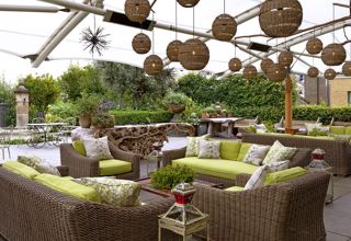 Diagonal shot from the bar of the Roof Terrace at Ham Yard Hotel, it shows the lime green cushioned and wicker sofa seating area with a coffee table in the centre. 