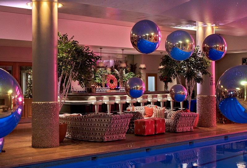 A shot from the pool that showcases the bar, the two sofas in front of it as well as large metallic looking baubles hanging from the ceiling.