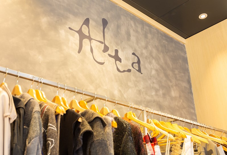 Clothes hanging on a railing in front of a wall grey wall with the 'Alta' logo on it.