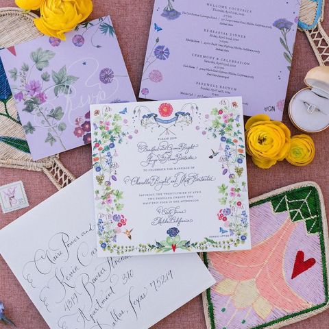 A collection of calligraphy work by Stephanie Fishwick, showcasing shades of purple and floral designs. Beside the illustrated pages are flowers and an engagement ring