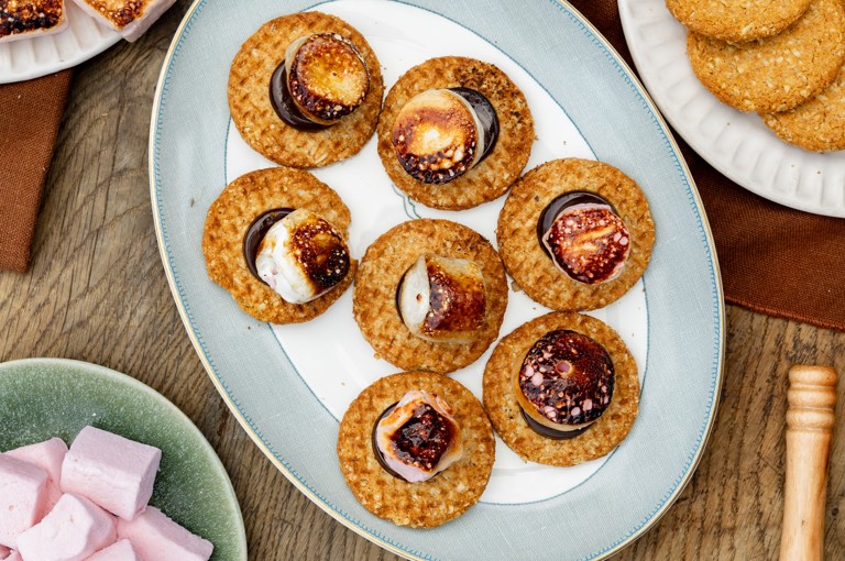 A selection of s'mores and their components sit on a selection of colourful plates on a wooden table